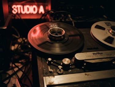Cinematic close-up of a vintage tape recorder reel spinning, warm tungsten lighting, heavy analog film grain, dark shadows, red neon reflection.