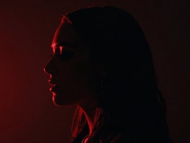 Moody cinematic film still, high-contrast chiaroscuro, a singer in deep shadow with a sharp red neon light outlining their profile, heavy film grain, 35mm lens