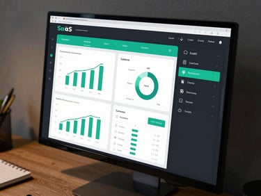 SaaS dashboard interface on monitor showing analytics charts and subscription data, dark mode UI with teal accent highlights, desk surface with notebook beside it