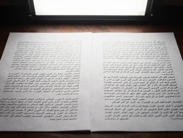 Arabic and English bilingual document side by side on a desk, close-up showing neat parallel columns of text, clean overhead studio lighting