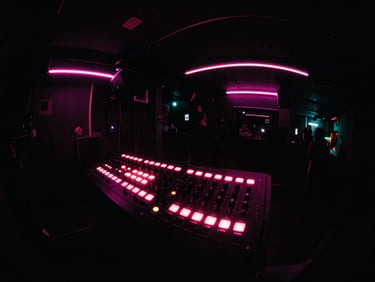 Album cover art with a fish-eye lens view of a blinking soundboard in a dark club, neon pink lights.