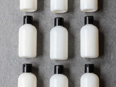 Structured flat-lay of minimalist hotel amenity bottles with matte black caps, soft natural daylight, slate gray background