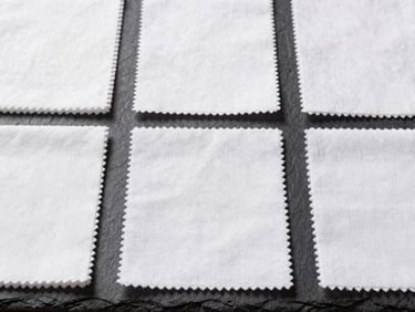 A structured flat-lay of white cotton fabric swatches neatly arranged on a dark slate surface, bright neutral daylight