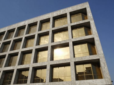 Low-angle architectural photograph of a completed multi-story commercial facade in Accra, sharp concrete angles, gold glass reflecting midday sun, 35mm.