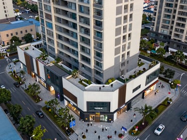 Aerial perspective of a mixed-use development at ground level showing completed retail base and residential tower above, pedestrians on surrounding streets confirming occupancy and scale