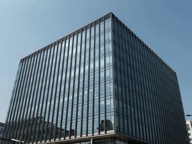 Wide environmental shot of a modern commercial office building exterior, glass curtain wall reflecting blue sky, architectural precision, midday daylight, no people