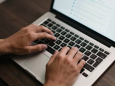 Close-up overhead view of hands typing on a laptop keyboard mid-configuration, a website layout visible on the screen, task lighting from above, dark desk surface beneath