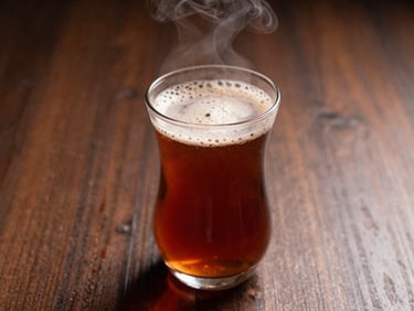 Freshly poured karak tea with rich foam in a traditional glass, steam rising, warm low-key lighting, 35mm