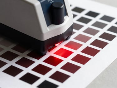 Close-up of a spectrophotometer calibrating color profiles on a freshly printed sheet of heavy paper stock, red light highlights