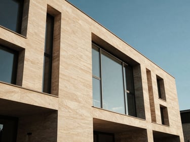 Façade d'une villa moderne habillée de pierre naturelle, lignes épurées, larges baies vitrées, ciel bleu clair, lumière vive, low-angle architectural shot, warm architectural photography, high-contrast editorial, 35mm