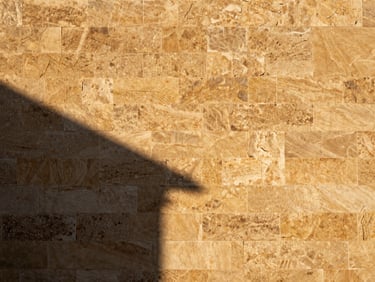 Vue détaillée d'un mur de façade en pierre de Taza, texture riche, lumière dorée du coucher de soleil, ombres portées, warm architectural photography, high-contrast editorial, 35mm