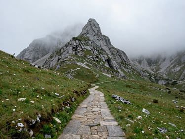 Overcast landscape of a narrow trail winding through the misty limestone peaks of Picos de Europa, green pastures, damp atmosphere.