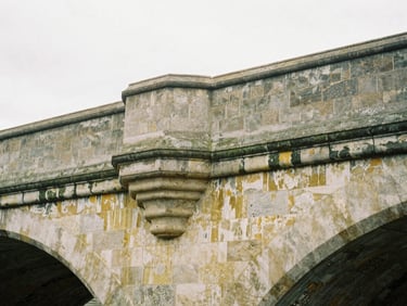 Close-up of weathered architectural masonry on an old stone bridge, soft overcast daylight, muted stone tones, 35mm film.