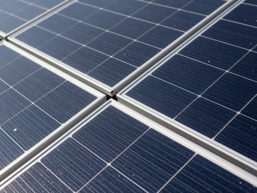 Close-up of a solar panel array, showing technical details and connections, under bright daylight. Industrial editorial photography, clean technical details, high contrast, deep slate and steel tones, 35mm.