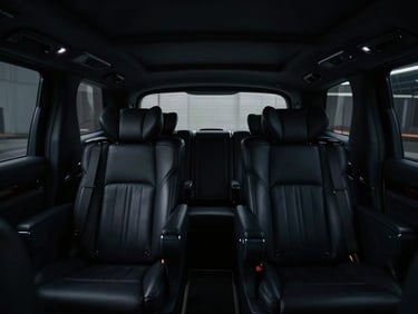Interior of a luxury private vehicle with dark leather seats and ambient lighting, seen from the back, showing a glimpse of a low-light terminal through the window, moody low-key lighting, deep shadows, cool dark tones, high-contrast, 35mm lens