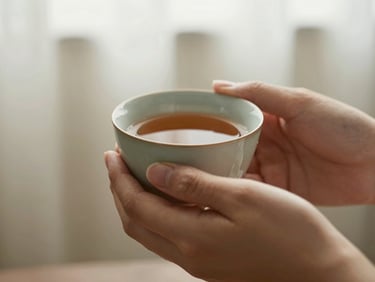 A close-up of hands holding a warm ceramic cup of tea, soft morning light, calm and grounding atmosphere