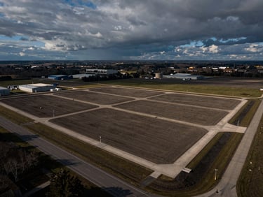 Aerial drone shot of a graded industrial land plot, clean boundaries, adjacent highway access, dramatic overcast sky