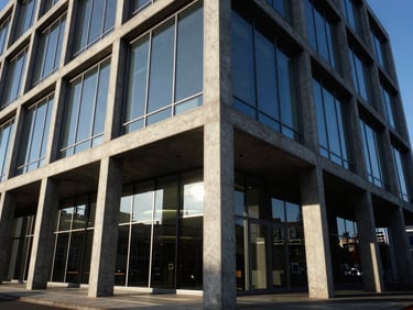 Exterior of a contemporary concrete and steel office building with large glass panels, sharp architectural angles, late afternoon sun