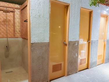 Rustic bathroom facility with bamboo shower stall and row of private wooden toilet doors.