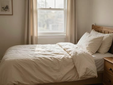 Warm residential board and care private bedroom with a sunny window, soft cream bedding, and a wooden nightstand.