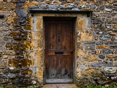 Detail of hand-dressed local stone around a newly installed timber door on a restored Yorkshire cottage, damp stone showing rich texture.