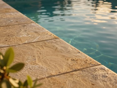 Close-up editorial shot of a private swimming pool edge with warm sandstone tiles, clear water reflecting the golden hour sky, soft green foliage nearby, shallow depth of field