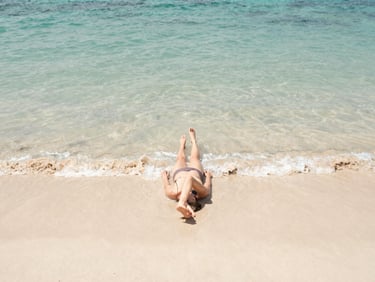 Authentic moment of someone relaxing on a clean, quiet beach with clear turquoise water, natural coastal daylight, warm desaturated tones, 35mm lens.