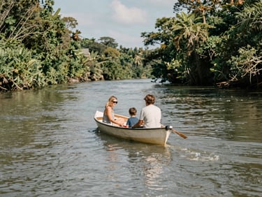 Authentic moment of a family (parents and child) enjoying a gentle boat ride on a calm river, lush green banks, natural coastal daylight, warm desaturated tones, 35mm lens.