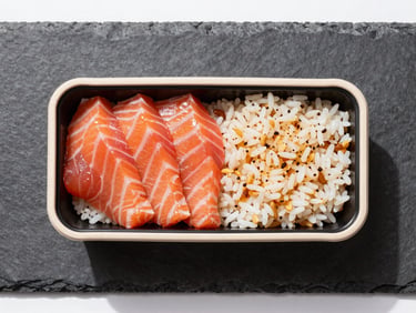 Overhead flat-lay of a modern bento box on a dark slate surface, bright natural daylight, sharp focus on fresh salmon sashimi and warm rice, clean minimalist styling, 50mm lens.