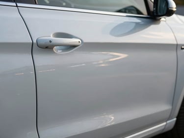 Car door panel post-repair gleaming under cool north-facing daylight, the previously dented area now flush and smooth, original factory paint reflecting light cleanly, close-up framing on the repaired surface