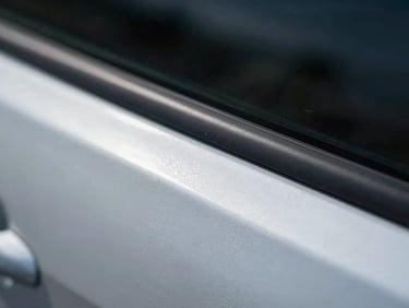 Extreme close-up macro shot of a car door panel dent edge under cool overcast daylight, the ridge of the dent casting a sharp shadow line across bare steel, no paint damage visible, technical documentation framing