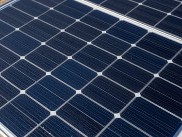 Close-up overhead shot of monocrystalline solar panel surface, blue-black cell grid with silver busbars, studio strobe lighting revealing precise cell geometry and anti-reflective coating texture