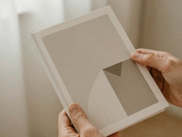 Close-up of hands holding a minimalist book with geometric cover art, warm diffused daylight, soft focus