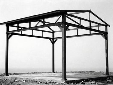 Historical black and white photograph of a demolished structural steel pavilion frame, harsh shadows, 35mm film grain