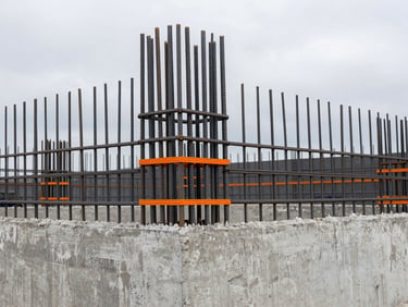 Technical close-up of steel reinforcement bars inside a concrete formwork, overcast day, desaturated tones, orange markings