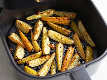 Overhead shot of golden roasted vegetables inside an open air fryer basket, realistic textures, natural lighting