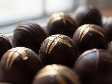 Close-up of a complex, glossy chocolate entremet with gold leaf decoration, dramatically side-lit, rich dark tones with gold accents, macro depth of field.