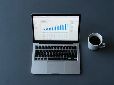 Clean overhead desk layout with a laptop displaying a financial report and a minimalist coffee cup, soft blue ambient light, desaturated navy and charcoal tones, sharp architectural focus, 35mm