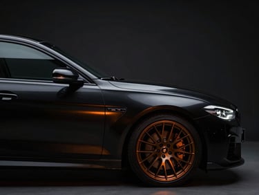 Vue de profil d'une berline sportive allemande noire brillante, éclairage studio dramatique, reflets orange sur la carrosserie métallique, jantes alliage sombres, flou d'arrière-plan, 50mm lens.