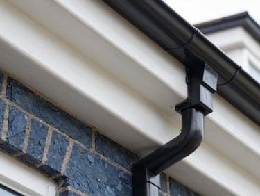 Tight macro shot of clean white UPVC fascias and black guttering installed on a brick home, bright daylight