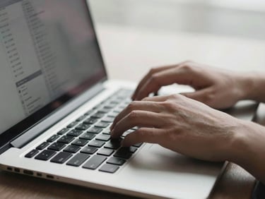 Close-up of hands typing on a laptop keyboard, data flowing on screen, soft natural light, desaturated cool tones.