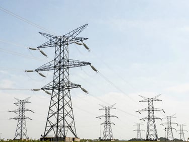Professional industrial photograph of large electrical transmission lines spanning a landscape, under bright natural daylight, clean technical details, high-contrast realistic tones, 35mm lens