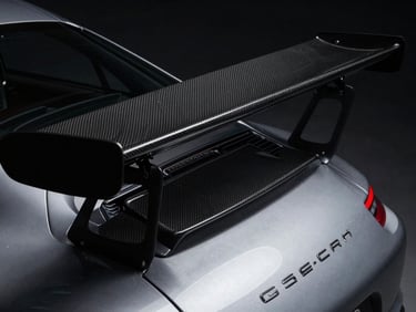 Tight macro shot of the carbon fiber wing and rear engine cover of a silver Porsche 911 GT3 RS, dramatic low-key automotive photography, moody studio lighting, deep shadows, high contrast, 50mm.