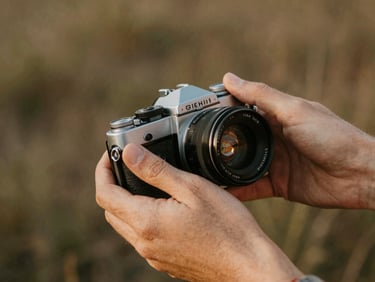 Close-up of hands adjusting a vintage camera lens in natural light, soft focus background, rich earth tones
