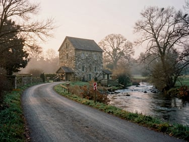 A scenic country road passing by a historic stone mill next to a slow river, golden hour lighting