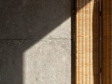 Architectural concrete wall with harsh direct sunlight casting sharp shadows, a rattan room divider detail showing rich natural weave texture, warm sandy tones, 35mm lens.