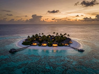 Aerial view of a tiny private tropical island at sunset, glowing villas, deep turquoise reef surrounding the white sand
