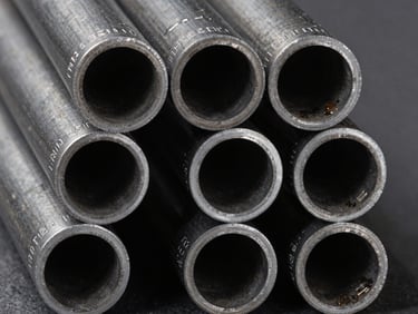 Macro overhead shot of carbon steel pipe ends arranged in a tight grid, grade markings visible on each pipe face, studio strobe lighting revealing wall thickness, dark grey surface