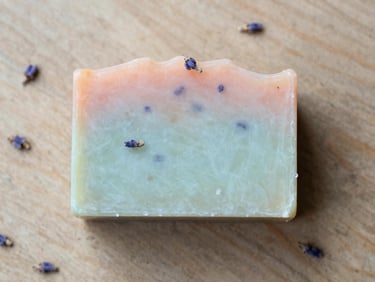 An artisanal solid soap bar with visible lavender buds resting on dry wood, overhead flat-lay