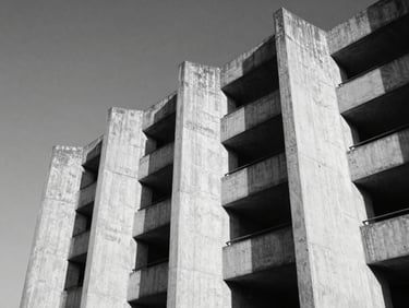 High-contrast black and white low-angle shot of brutalist concrete architecture in Accra, hard midday sun casting sharp geometric shadows, negative space on the left.